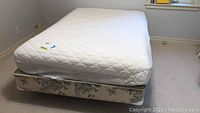 Metal bed frame shown supporting a mattress and boxspring; mattress is white quilted and boxspring is floral patterned