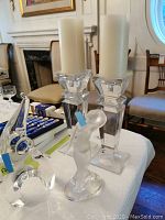 Two carved clear glass candlestick holders, frosted female figurine and clear elephant sculpture arranged on table