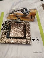 Photo showing the headset in packaging beside the Michael Aram hammered metal candy dish with floral decoration on the corner.