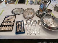 Wide view of all silverware items on table including boxed cutlery sets, serving trays, chafing dish and cream set.