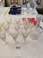 Front angled view of 9 crystal wine glasses and the matching decanter with cross and olive cut pattern on a table.