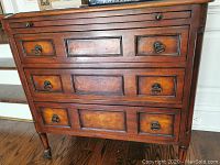 Front view of wooden cabinet showing three drawer fronts and brass ring pulls