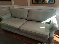 Front angle photo of light green upholstered sofa showing cushioning and wear.