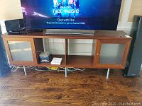 Full front view of the wood TV credenza with compartments and glass shelves. A TV and soundbar placed on top for scale reference.