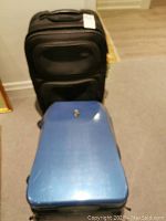 Two medium luggage pieces on wheels, one blue hard-shell Heys case and one black soft-shell Samsonite case.