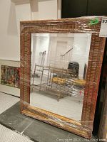 Wood framed mirror wrapped in plastic, showing carved geometric patterned frame and clear mirror surface.