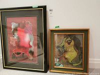 Two framed art prints, one abstract and signed, the other a cat illustration, both leaning against a wall.