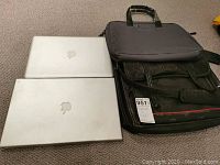 Photo showing two MacBook Pro laptops and two laptop bags on a carpeted floor, with Apple logos visible on laptops and details of bags apparent.