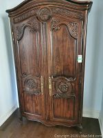 Front view of the ornate carved oak armoire showing two doors and curved bonnet top