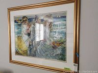 Side angled photo of the framed print showing three women by the sea in colorful dresses with boats in background