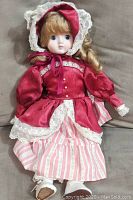 Front view of the vintage porcelain doll seated on a couch, showing dress details and face.