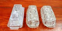 Top view of three clear glass butter dishes with lids on a wooden surface.