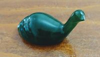 Top and side view of a small carved dark green jade bird with smooth polished surface and simple shape.