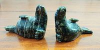 Photo of two green soapstone seal sculptures laying on their backs showing belly and flipper details