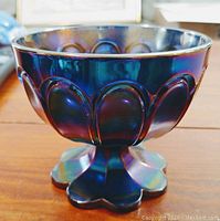 Side angle image of the blue and purple iridescent carnival glass candy bowl showing scalloped pattern and pedestal base.