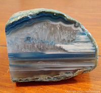Front face of the polished agate showing blue, white, gray banding and crystal formations.