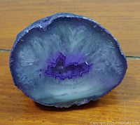 Close-up photo of a polished agate slice with purple and gray banding on a wooden surface.