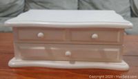 Closed white wooden jewelry box showing front with three knobs and base with smooth lines.