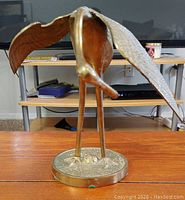 Front view showing elongated legs, wings, and rounded base of the brass heron statue.