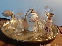 Overview of brass tray holding six vintage perfume bottles of various styles and a glass bell, showing arrangement and details of design.