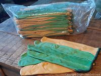 Stack of twelve pairs of gardening gloves wrapped in clear plastic packaging on wooden surface with two pairs laid out in front.