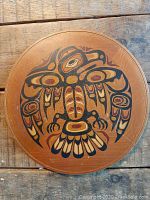 Front of wooden plate showing stylized Indigenous eagle design painted in black and red on cedar wood surface.