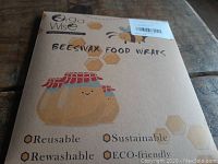 Front of package showing brand Oga Wise, product name BEESWAX FOOD WRAPS, and product features reusable, washable, sustainable, eco-friendly.