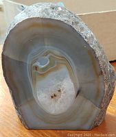 Front view of a polished gray and brown agate with banding and crystal center.