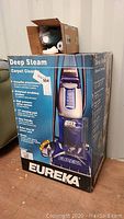 Image of sealed original box showing front and side views of the Eureka Deep Steam Carpet Cleaner with motorized scrubbing brushes, 12-inch cleaning path, 32-foot power cord, and bonus cleaning concentrate.