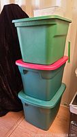 Three green Sterilite storage totes stacked, one with a red lid