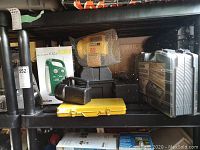 Shelving unit with several items including various tool and tackle boxes, yellow ratchet set case, black flashlights, metal toolbox and boxed radio lamp