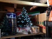 Photo of large and smaller ceramic Christmas trees, multiple tins including Wedgwood cookie tin, glasses with tree designs.