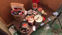 View of multiple vintage tin containers and catalogs arranged on a table, showing part of the lot.