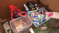 Collection of Spiderman items, Batman comic, tabletop baseball game, and boxed Hot Wheels cars and other small toys in tote bins.