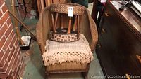Wicker rocking chair with two foot stools stacked on seat, showing woven texture and cushion detail.