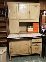 Overall front view of two-piece painted wood Hoosier cabinet with enamel countertop and stacked wooden boxes