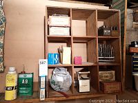 Wooden nine-hole cubby with various items including drill bits, metal stamps, cutting fluids, and boxes.