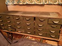 Full view of metal storage cabinet with multiple small drawers closed, showing worn green paint and aged metal surface.
