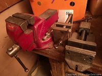 Wide view of all three bench vices mounted on a wooden bench showing relative sizes and condition