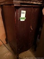 Full view of the front and side of the wooden record cabinet showing two doors, keyhole, and cabinet leg with threshold wear and surface scratches.