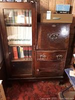 Front view of the antique wooden secretary desk showing glass cabinet with books inside and drawers on the right.