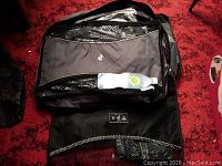 Black and grey double decker packing cube with mesh compartments and a tag visible on red carpet.