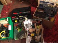 Boxes and containers of assorted hand tools, screwdriver sets, electronic meter, work light, and hardware items packed together.