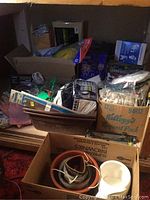 Wide view showing multiple open boxes filled with assorted hardware and garden items including gloves, cords, shelf brackets, and lights.