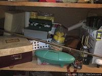 Shelf containing a box with sewing machine accessories, a turquoise plastic case, and other miscellaneous items.