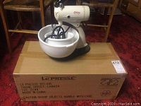 Mid century Sunbeam Mixmaster on stand with two white plastic bowls and cords visible, sitting on cardboard box containing LePresse juicer press.