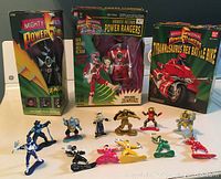 Photo shows a collection of small Power Ranger action figures arranged in front of three large boxed figures (Zack, Jason, Red Ranger) and an unopened boxed Tyrannosaurus Rex Battle Bike with Red Ranger.