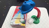 Image of the trace and draw projector unit with green suction cup base and a white projection wheel beside it, placed on top of a table with original box in background.