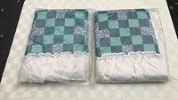 Two green patchwork pillow shams folded and in original clear packaging shows checkered pattern with white ruffled edge.