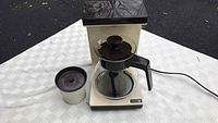 Full view of vintage Norelco drip coffee maker base with glass carafe and detached filter basket on table.